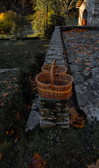 Two empty wicker baskets for collecting mushrooms on a stone wall in an autumnal setting near an old farmhouse.