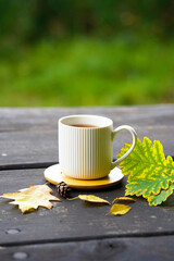 A cup of tea standing on a wooden table,next to the cup are autumn leaves and a pine cone,which creates an atmosphere of coziness and autumn