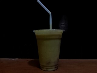 Frothy green beverage in a transparent cup with a straw against a dark background