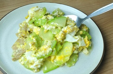 Spoon scooping traditional medicinal angled luffa and egg stir-fry. It acts as a cooling diuretic and milk booster for postpartum health.
