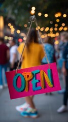 Colorful handwritten OPEN sign hanging on a glass window with blurry crowd in background