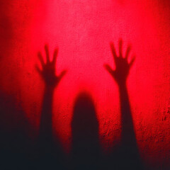 Shadow hand silhouette on red textured background creates creepy and eerie atmosphere with sense of being trapped or reaching out in fear