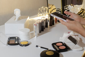 Woman holding phone at the cosmetics store, near makeup display counter and choosing right product. Compare and buying beauty products