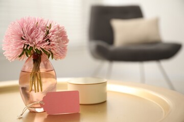 Blank card, vase with flowers and candle on table indoors. Space for text