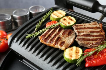 Electric grill with beef steaks, vegetables and rosemary on grey table, closeup