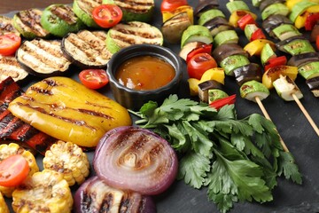 Vegetarian barbecue. Tasty grilled vegetables, parsley and sauce on black table, closeup
