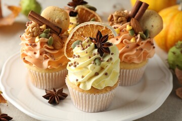 Delicious cupcakes with colorful cream, spices, cookies, nuts and autumn decor on table, closeup