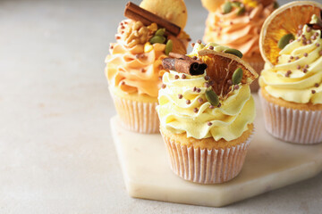 Delicious cupcakes with colorful cream, spices, cookies and nuts on grey table, closeup. Space for text