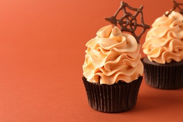 Delicious cupcakes with chocolate web on coral background, closeup with space for text. Halloween celebration