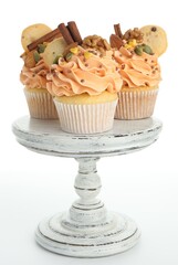Delicious cupcakes with sprinkles, spices, cookies and nuts on stand against white background. Autumn atmosphere