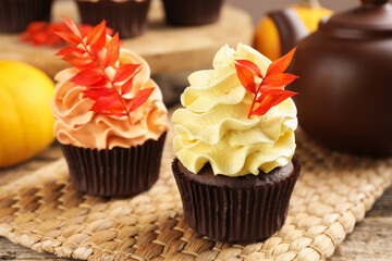 Delicious cupcakes with branches with red leaves on wooden table, closeup. Autumn atmosphere