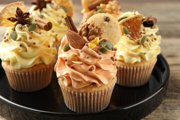 Delicious cupcakes with sprinkles, nuts and spices on wooden table, closeup. Autumn atmosphere