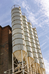 Row of tall white industrial silos against blue sky beside red brick factory building