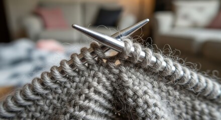 Close-up of knitting needles and grey yarn on cozy sofa