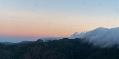 A mountain range under a pastel sky with clouds covering the peaks at dusk in a scenic landscape © Rodrigo