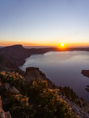 Sunrise over crater lake oregon with mountains and trees in the foreground and clear sky above lake