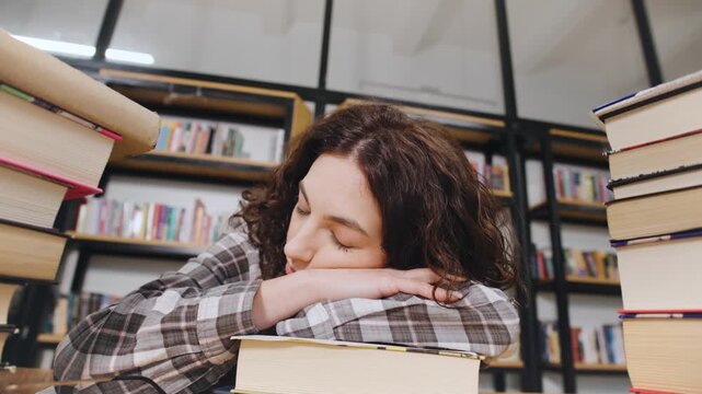 Female curly Student resting on desk surrounded by books in library during study session