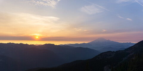 Sunset view over layered mountains with a hazy horizon and a pastel sky filled with soft clouds © Rodrigo