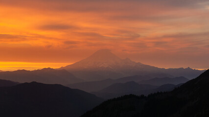 Silhouette of mountain range against a vibrant orange and yellow sunset sky with soft clouds above