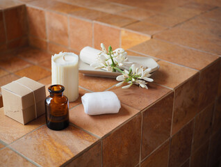 White candle amber bottle white towel and white flowers on terracotta tiles