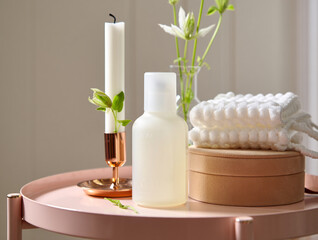 White candle in copper holder next to lotion bottle and towels