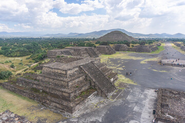 Side view of ancient pyramids at Teotihuac&aacute;n, an iconic archaeological site in Mexico. The image shows the vast stone structures under a cloudy blue sky.