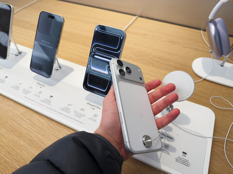 Holding a modern iPhone 17 Pro in a tech store with display models and accessories
