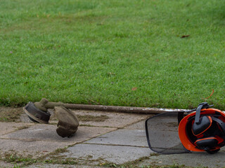 Orange safety helmet and brush cutter resting on paving stones after lawn maintenance work