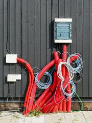 Outdoor electrical installation with red conduit pipes, wires, and fuse box on black wall