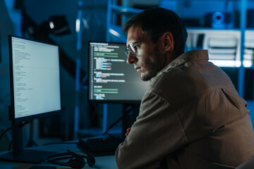 Caucasian IT engineer coding in dark office, working on cybersecurity, hacking prevention, and modern digital security solutions.