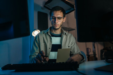 Caucasian programmer coding in dark office, focusing on IT solutions, cloud computing, and software development tasks.