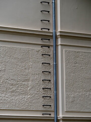 Vertical lines of safety rungs and a downspout against a textured beige facade