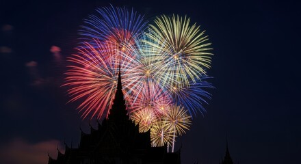 Fireworks Bursting Over Silhouette: A vibrant display of colorful fireworks illuminates a serene nighttime sky, cascading above a silhouetted structure.