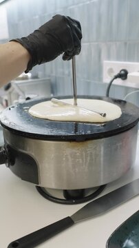Chef spreading crepe batter on hot griddle