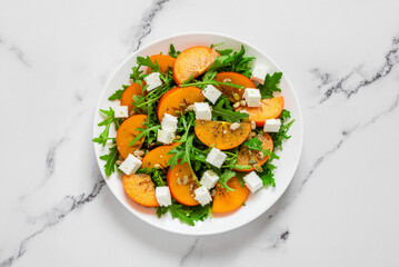 Persimmon salad on a white plate on a marbled surface, top view