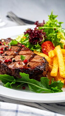 Close-up of a grilled beef steak served with french fries and fresh salad on a plate. Delicious gourmet meal for dinner or lunch, concept of tasty and balanced cuisine.