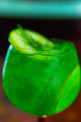 A vibrant green cocktail is presented in a stylish glass, garnished with cucumber and herbs, perfect for summer.