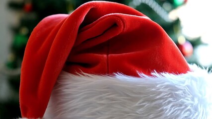 Close-up shot of a red and white velvet Santa hat with a soft fur brim on a blurry background with Christmas tree decorations - Powered by Adobe