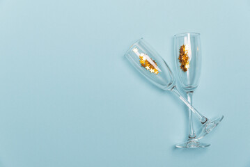 Champagne Glasses for New Year party with Gold Ornaments and Star Confetti on Blue Background