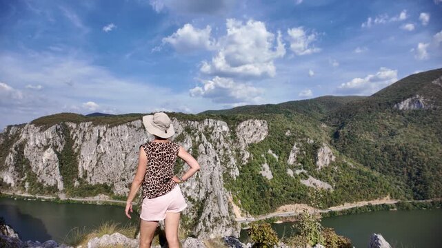 Woman sitting on rocks, enjoying the expansive panoramic view of the Danube river gorge and forested mountains in the Djerdap National Park at the border of Serbia and Romania