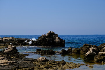 Rocky coastline with rock formations meeting turquoise sea under blue sky