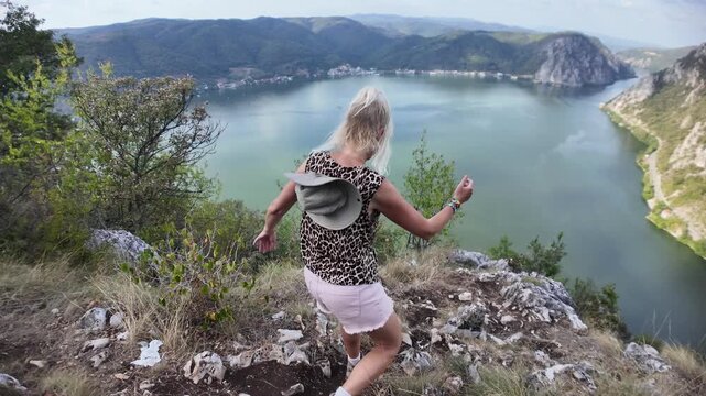 Woman standing on a rocky viewpoint, admiring the scenic Danube river winding through the rugged gorge and towering cliffs on the border of Serbia and Romania, enjoying nature and a clear sky