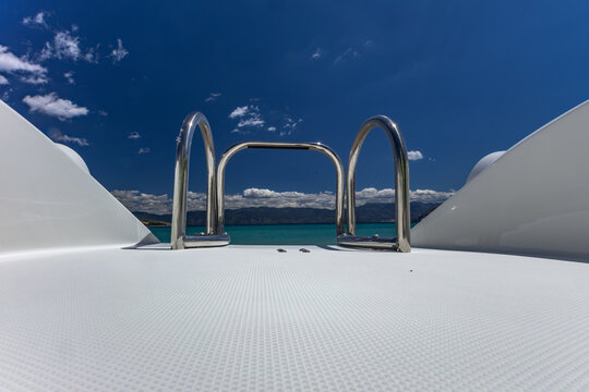 Scenic panoramic view of Baska Bay with turquoise Adriatic Sea, marina, sandy beach, and coastal town surrounded by rocky mountains on Krk Island, Croatia, under a clear blue sky
