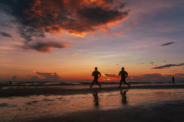 Fototapeta premium Silhouettes of two men running along a beach at sunset