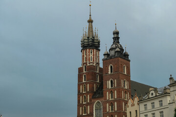 Fototapeta premium The iconic twin towers of St. Mary's Basilica, a masterpiece of Gothic architecture, majestically rise against a dramatic, overcast sky in Krakow's historic Main Market Square, Poland.