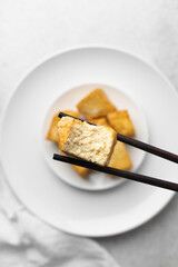 Overhead view of fried tofu in chopsticks, top view of pan fried soya bean tofu cubes