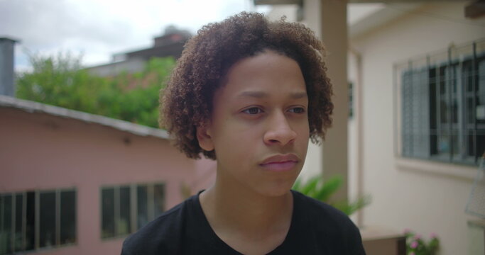 Latino teenage boy from African descent with a serious expression standing outdoors in a Latin American residential neighborhood, conveying thoughtfulness and introspection