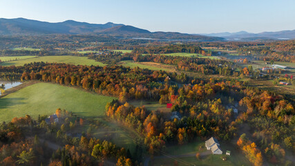 Foggy autumn sunrise over colorful farmland, trees, and rolling hills in Stowe, Vermont.