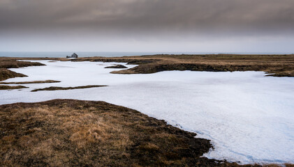 Serene winter landscape featuring melting snow and distant cabin in Iceland