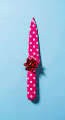 Knife Wrapped in Pink Polka Dot Paper with Red Bow on Light Blue Background for Festive and Conceptual Visual Contrast
